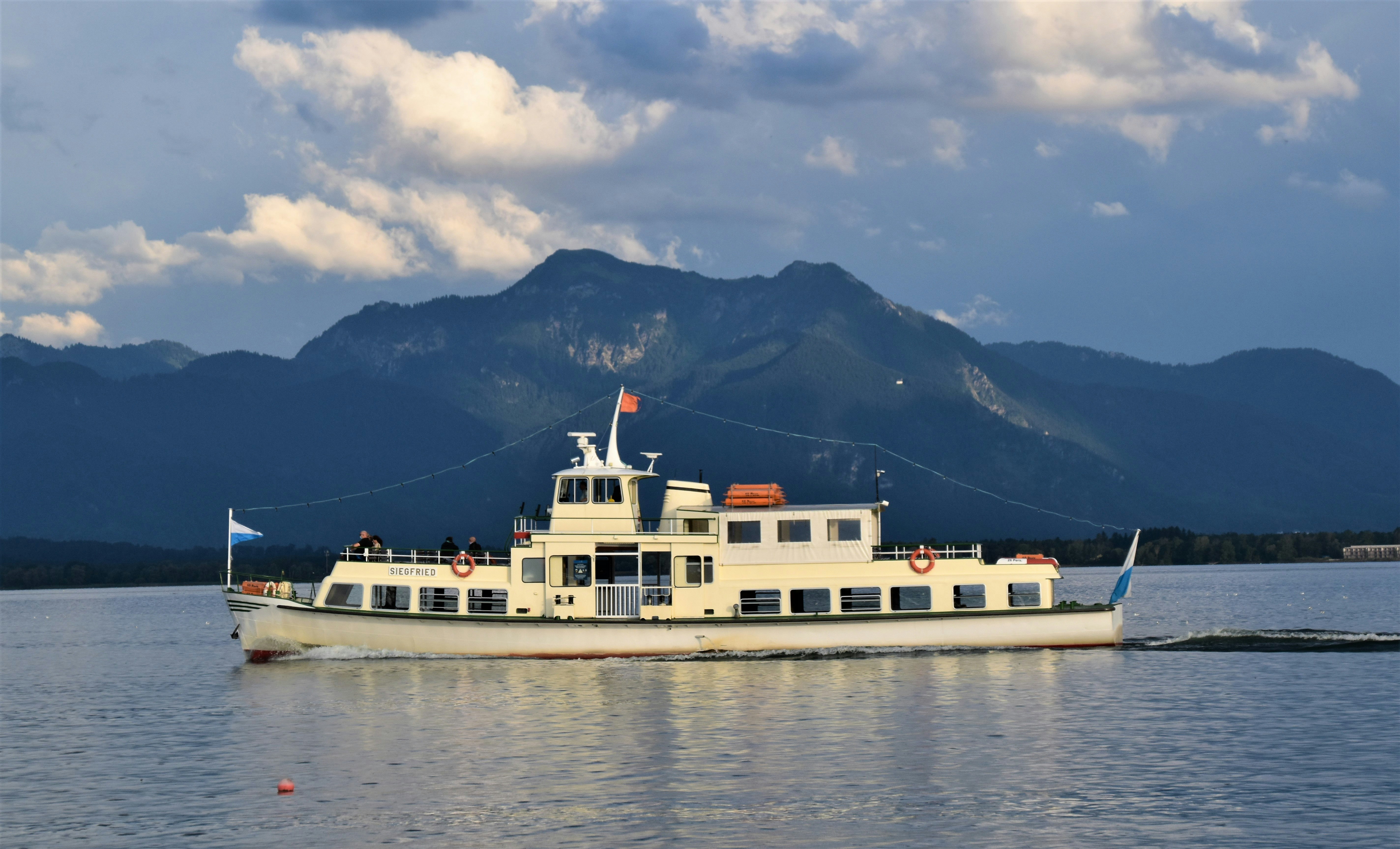 white ship on sea near mountain under cloudy sky during daytime